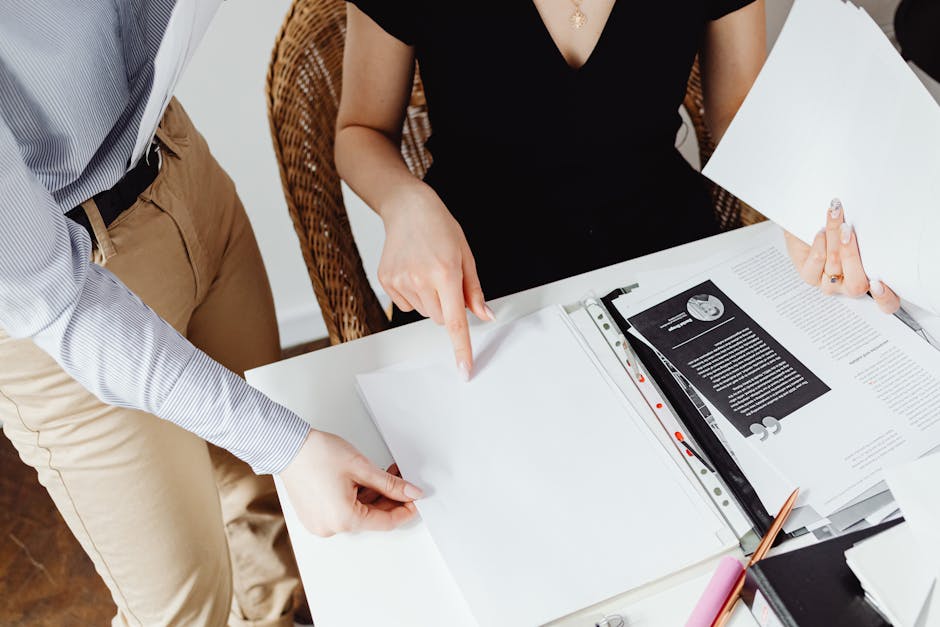 Two colleagues working together on documents, pointing and discussing details.